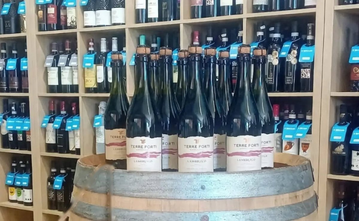 Bottiglie di Lambrusco su una botte, davanti agli scaffali dei vini dell’enoteca Il Bibitaio